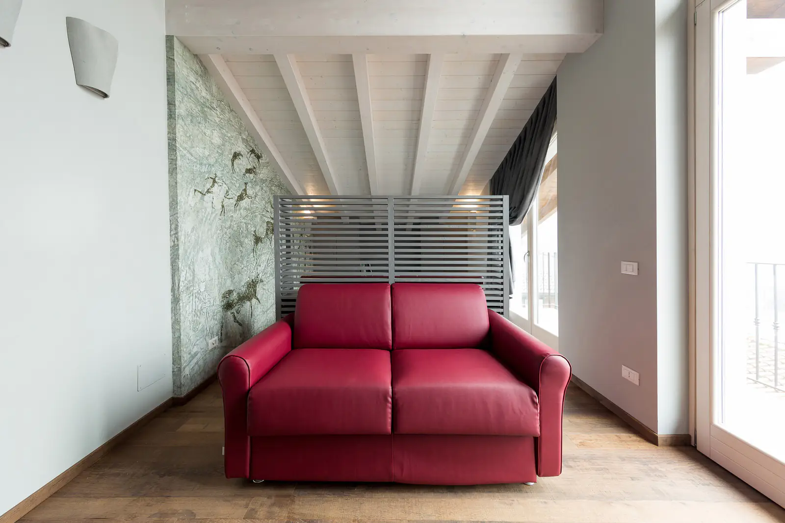 Suite Camuni – Camera con divano rosso e parete decorata